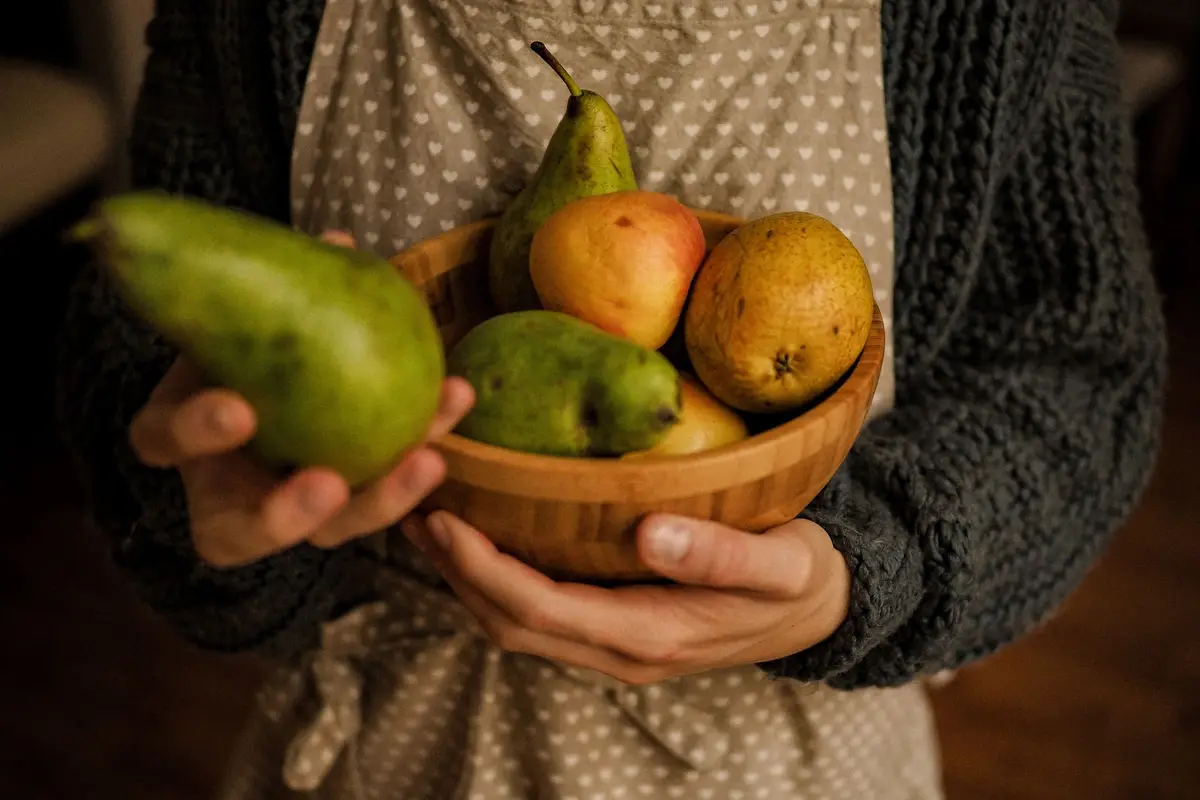 Iemand met een schort voor houdt een houten schaal met peren en appels vast